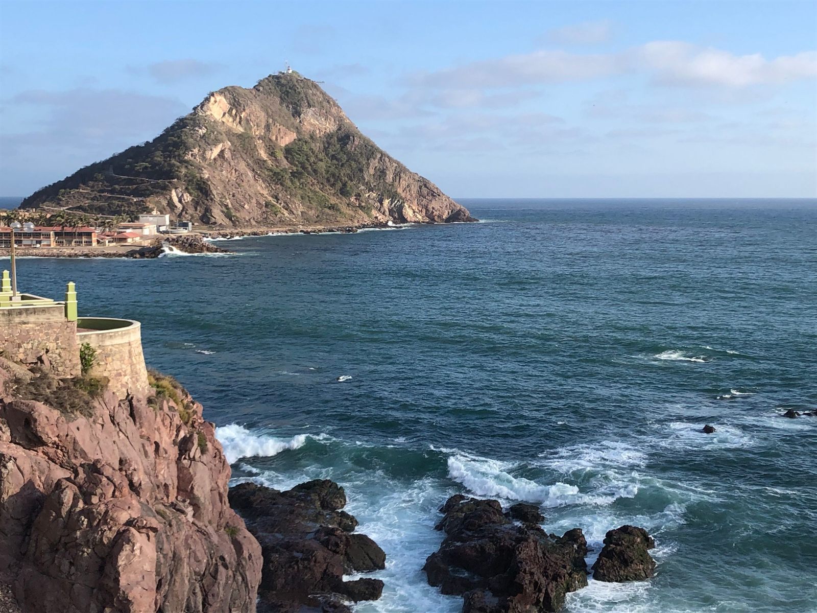 Waves breaking on dark rocks below a lighthouse hill on the Pacific coast of Mexico